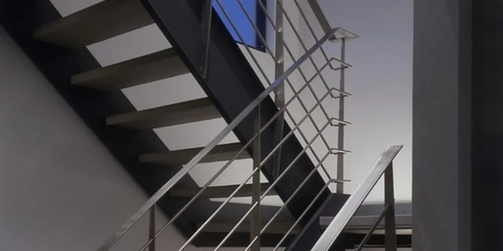 A sleek interior staircase with minimalist metal railings and large windows marries modern design with functionality, allowing natural light to enhance the staircase's airy, open ambiance.