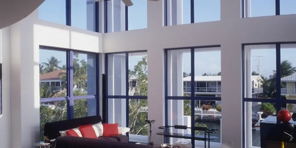 A living room with soaring, light-filled windows invites the beauty of natural surroundings inside. The interior mixes comfort with modernism, encouraging both relaxation and social enjoyment.

