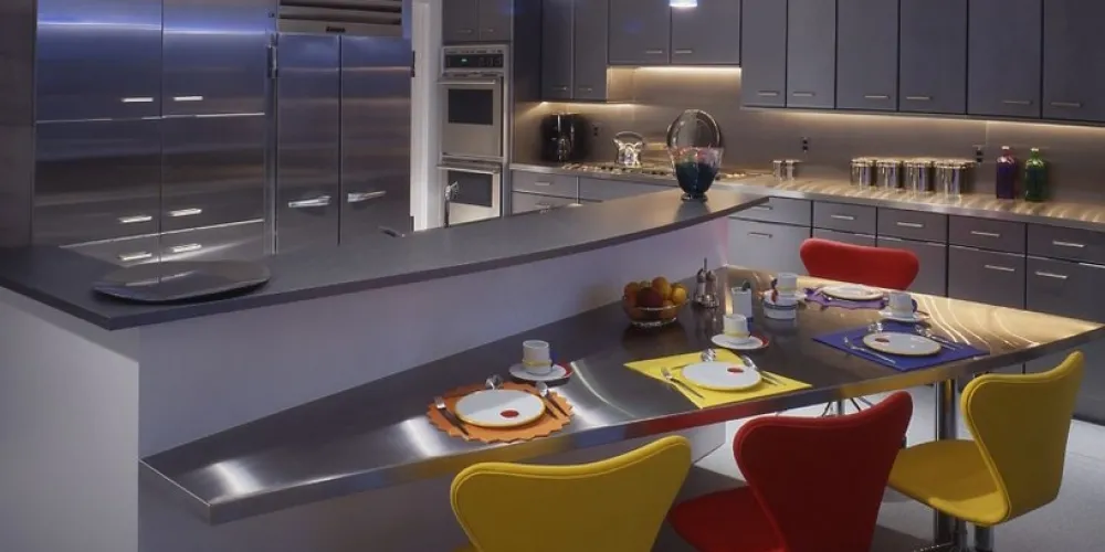 The kitchen showcases sleek stainless steel appliances with vibrant, playful seating against contemporary cabinets. Modern lighting highlights the chic design, marrying functionality with flair.

