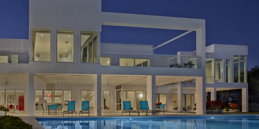 This image showcases the home's impressive exterior at night, with its clean, geometric lines illuminated by strategic lighting. The expansive terrace and pool area provide an inviting, serene atmosphere, highlighting the architectural symmetry.
