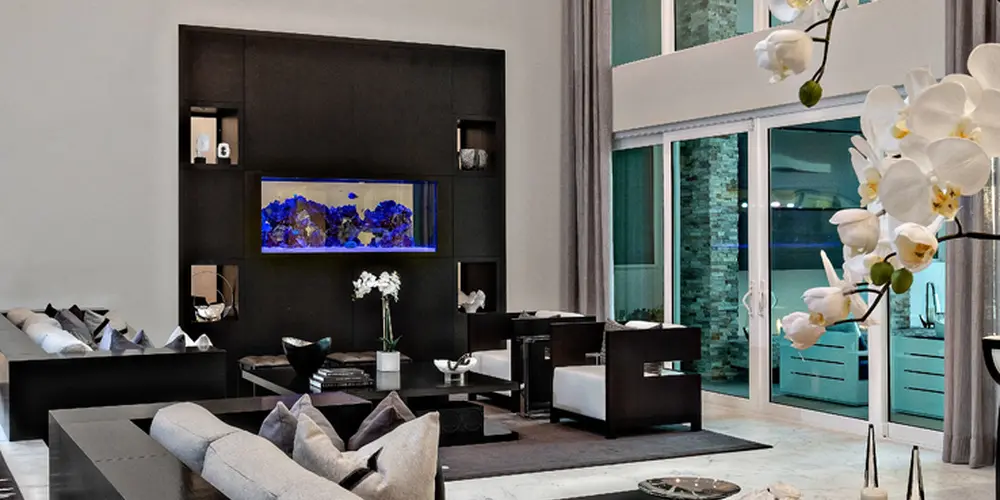 The living room features lofty ceilings and floor-to-ceiling windows, creating a spacious and airy environment. The minimalist yet luxurious decor, including plush seating and a chic chandelier, provides a sophisticated atmosphere.