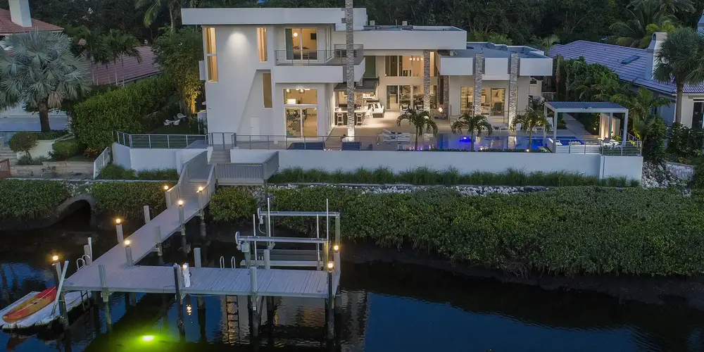 This aerial perspective showcases the home’s modern geometric design, set perfectly against the serene waterfront. The multi-level architecture, adorned with expansive windows, maximizes the picturesque views and outdoor spaces.