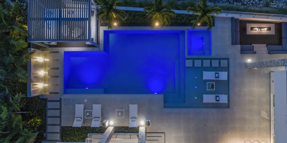 The bird’s eye view of the pool area showcases nighttime illumination that enhances the space's elegance and functional design. Clean lines and modern detailing around the lounge areas reflect a luxurious, inviting outdoor experience.