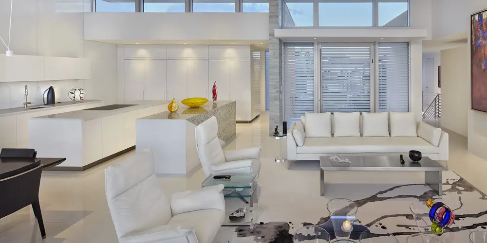 The living room blends minimalist decor with high ceilings and expansive windows, maximizing light and space. White furnishings and bold artwork create a sense of modern sophistication and comfort.