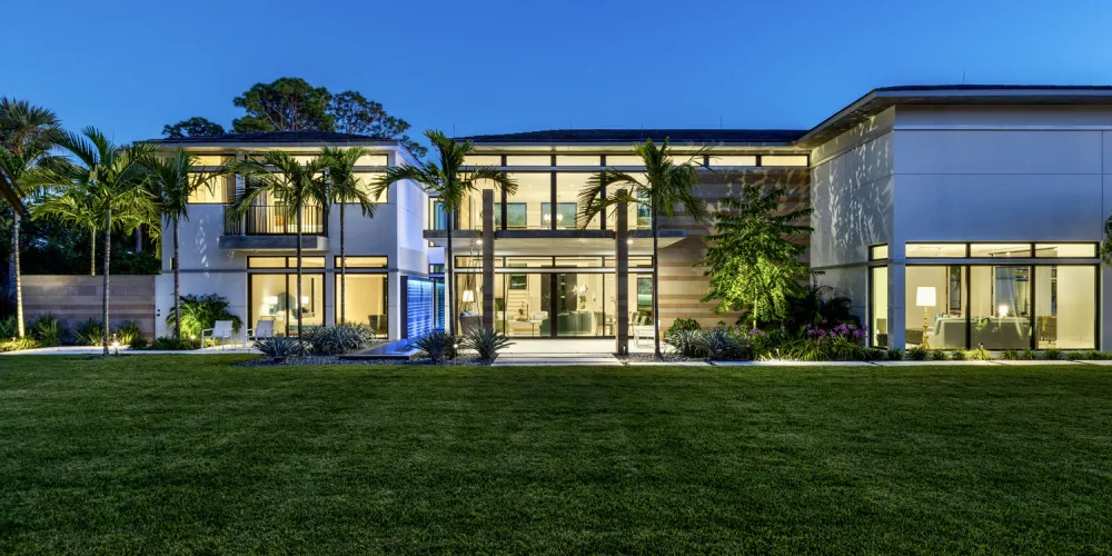 The home's striking evening presence is highlighted by extensive glass walls and strategically placed lighting. The illuminated interior contrasts with the night sky, enhancing the home's contemporary elegance.