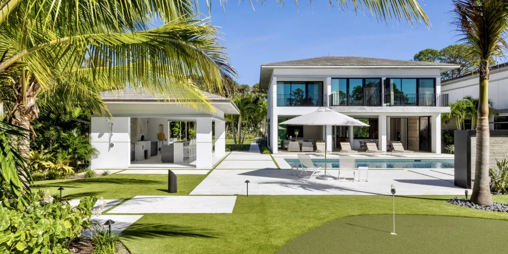The backyard is equipped with outdoor amenities including a putting green and poolside lounging, offering a luxurious extension of living spaces designed for leisure and entertainment.