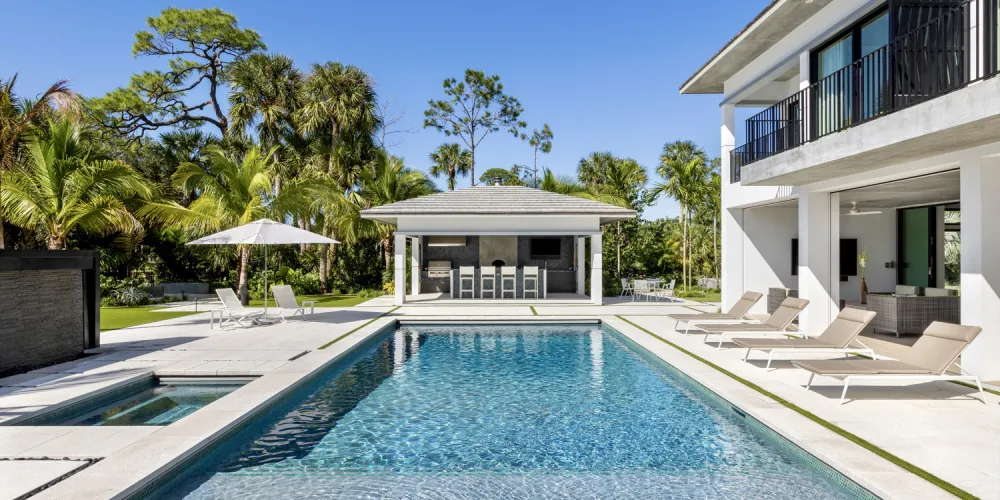The poolside area is enhanced by a shaded outdoor bar and lounge, providing a functional and stylish space for entertainment. The integration of natural elements and sleek architecture offers a seamless flow between indoor and outdoor living.