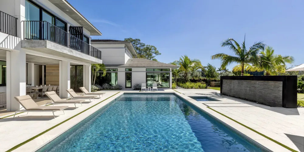 The pool area is a central feature of the outdoor space, with clean, geometric lines and a spacious deck for sunbathing. The use of light-colored materials enhances the reflective quality of the water, creating a bright, inviting environment.
