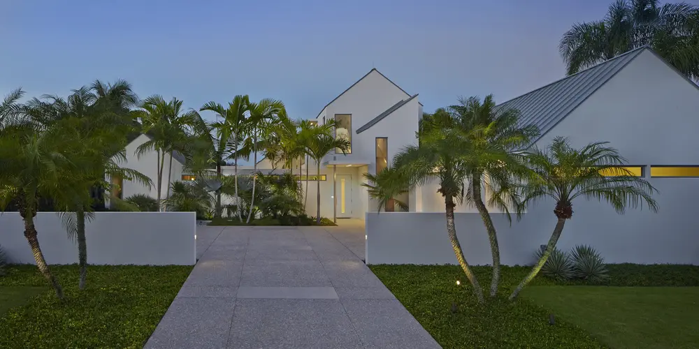 Architecture: This image captures the front facade's contemporary design, featuring crisp white walls, steep rooflines, and lush landscaping. The driveway and entrance are lined with elegantly arranged palm trees.
