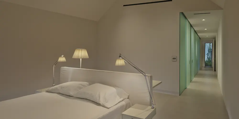 This image highlights a minimalist bedroom featuring clean lines, neutral tones, and integrated lighting. Elegance is emphasized by the vaulted ceiling, offering a sense of spaciousness and tranquility.