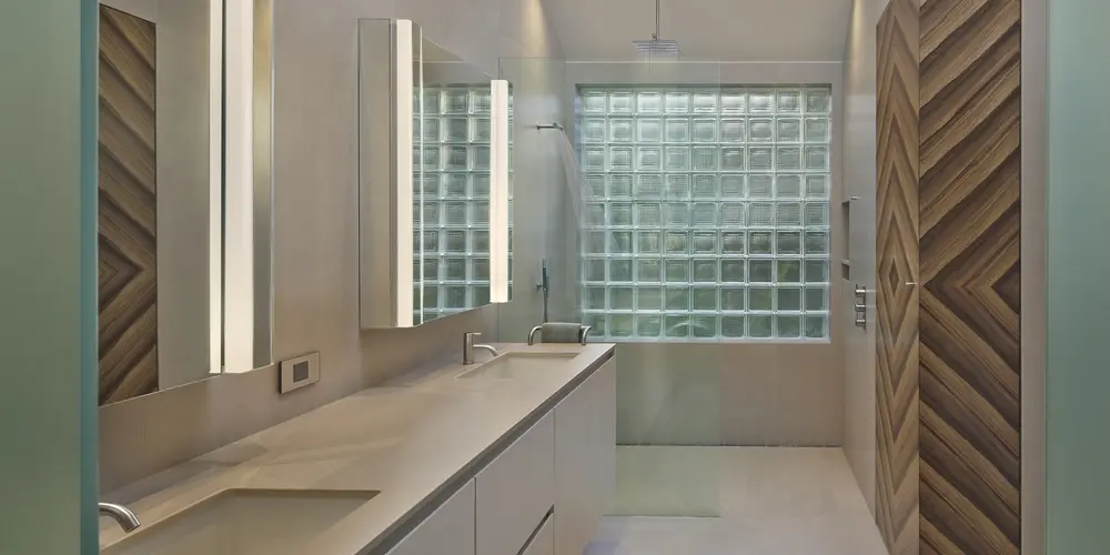 The bathroom features a sleek design with textured wood accents and frosted glass walls, creating a refined and luxurious atmosphere. Integrated lighting enhances the sophisticated aesthetic.