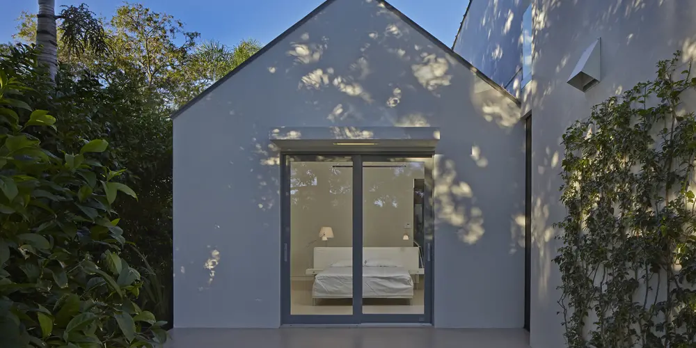 The rear view offers a glimpse into the well-lit interior, highlighting the home's simplicity and elegant design. Large glass doors frame the room elegantly with views to the backyard. 
