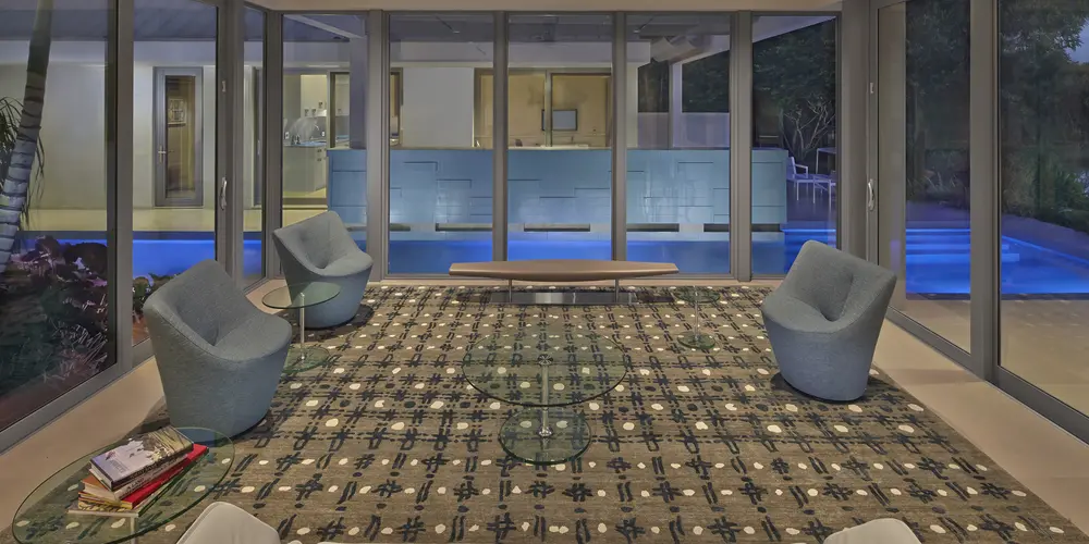  The lounge area offers panoramic views of the pool through expansive glass walls. Plush seating and a patterned rug provide comfort and style.
