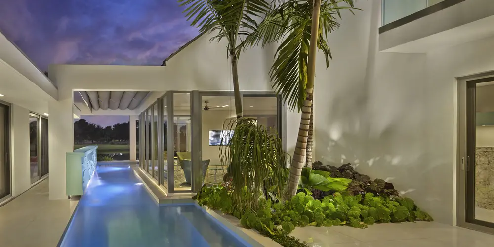 The poolside at dusk creates a tranquil oasis, with accent lighting highlighting architectural features and lush greenery. The pool's reflective surface amplifies the serene ambiance.

