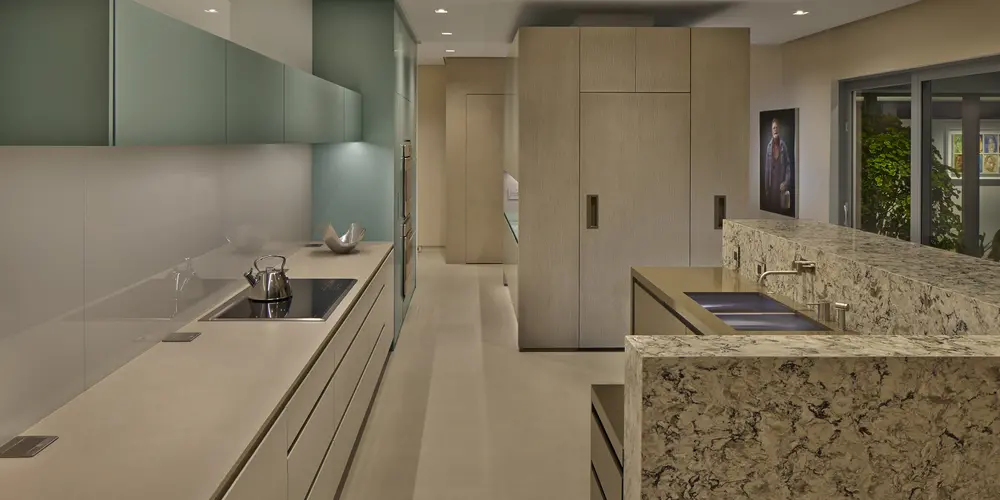 The kitchen features a minimalistic design with integrated cabinetry, textured stone surfaces, and muted color palettes. The layout is both functional and elegant, embodying contemporary sophistication.