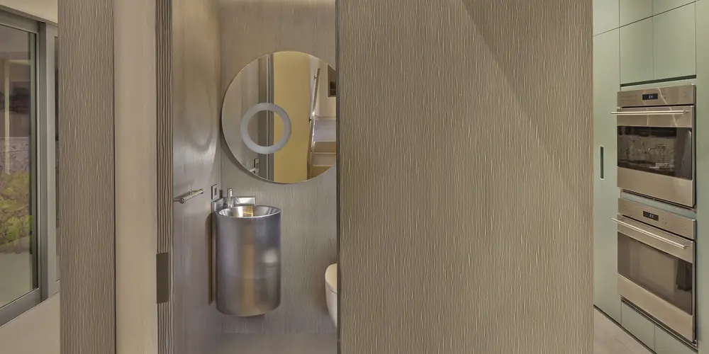 The powder room is a compact yet stylish space with round mirrors and sleek materials, featuring a modern color palette. The room's design highlights functionality without sacrificing elegance.
