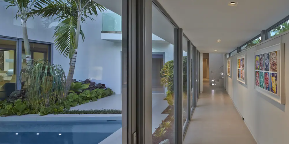 This glass corridor not only connects spaces but also showcases the pool and garden, allowing natural light to penetrate while framing the lush views, enhancing the home's open and airy feel.
