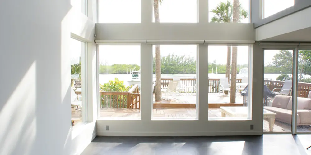 This space features a dramatic double-height room with expansive windows that flood the area with natural light. The floor-to-ceiling glass provides a direct visual connection to the outdoor environment, enhancing the sense of openness and continuity between indoor and outdoor living spaces. The use of large square tiles complements the airy atmosphere, maintaining a streamlined modern aesthetic.

