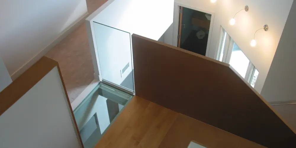 This perspective captures the top view of the staircase, revealing its interior connectivity. Wood and glass components emphasize lightness and accessibility, enhancing the architectural flow. The glass bridge section separates the master bedroom from the upstairs office loft. 