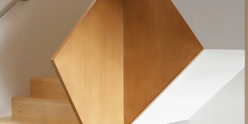 A close-up of the staircase accentuates its precise craftsmanship and use of natural wood. The angular form reveals complexity and elegance, contributing to the home’s contemporary aesthetic.
