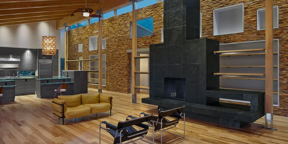 The room's open-concept layout features high ceilings with exposed wooden beams, contributing to a sense of expansiveness and warmth. A prominent dark stone fireplace serves as a striking focal point, adding both visual interest and functional benefit. The natural stone surface contrasts with the light wooden flooring, creating a harmonious balance of color and texture within the space.
