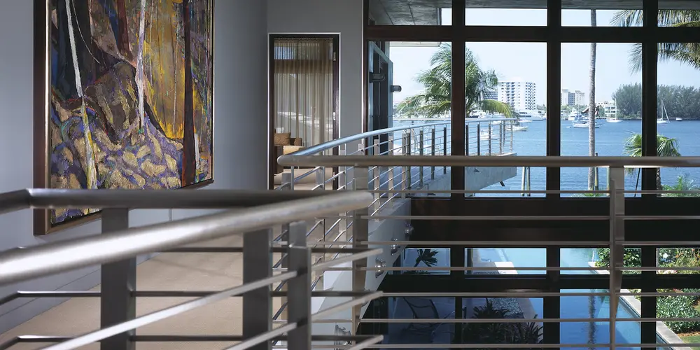 This space features sleek full-height windows that seamlessly connect the interior with the outdoor landscape, providing expansive views. The stainless steel railings add a modern industrial touch that complements the minimalist design.