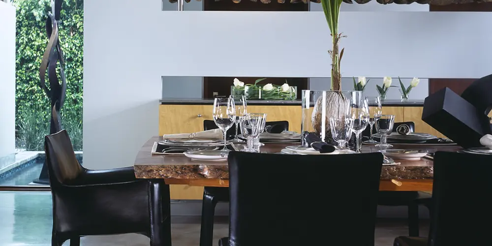 The dining area combines a rich wooden table with sleek black chairs set against a polished concrete floor, offering a balanced blend of modern and natural aesthetics.