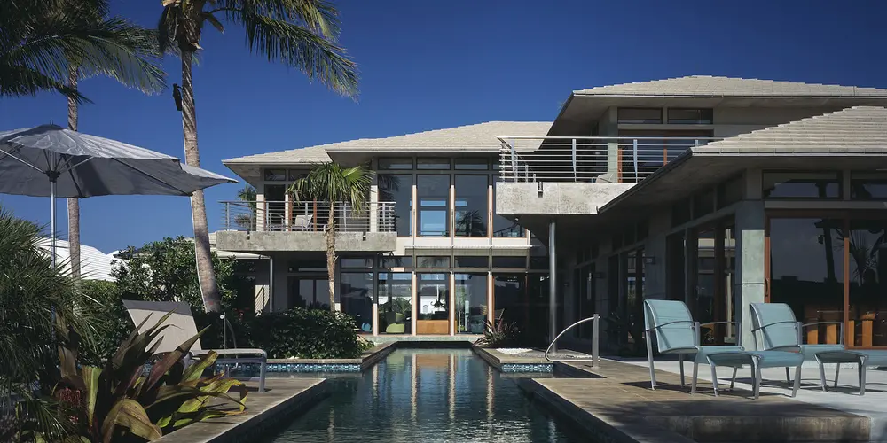 The pool area reflects serene sophistication with tropical landscaping and luxurious seating arrangements. The use of mosaic-tiled pool surfaces adds texture and vibrancy to the outdoor space, creating an ideal setting for relaxing or entertaining.
