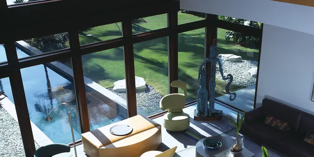 The lounge area features open, floor-to-ceiling windows that frame picturesque water views. Vibrant furnishings and varied seating arrangements promote relaxation, while a mix of artistic pieces adds character and playfulness to the airy, light-filled space.